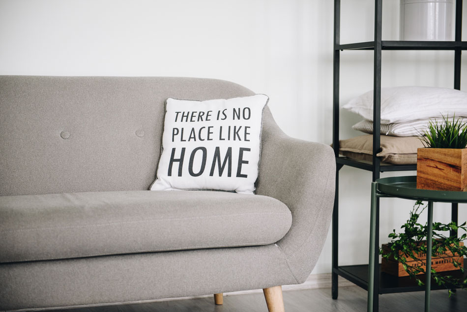 Ein Sofa mit einem kleinen Tisch daneben und einem Kissen mit der Aufschrift: "There is no place like home"